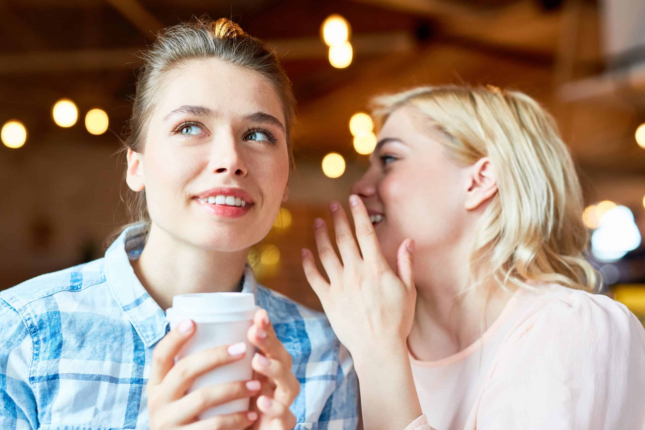 Young blonde whispering curious news in her friend ear at coffee break